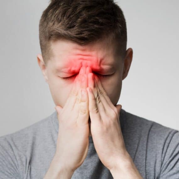 A man holds his hands to his face, with a red area highlighted on his forehead and nose, suggesting sinus pain or headache—an image that raises the question of when to suspect chronic sinusitis.