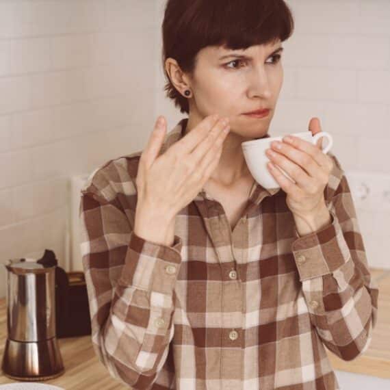 Woman sniffing coffee in the kitchen. Illustrates Long COVID ENT symptoms including anosmia (loss of smell), parosmia (distorted smell).